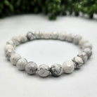 White faceted howlite beaded bracelet on a white surface with a blurred green background