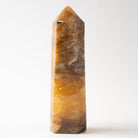 A polished natural Golden Healer quartz crystal point with marbled patterns of golden yellow, amber, and dark brown, standing upright on a white background.