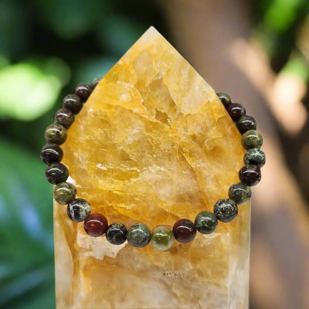 Dragon Bloodstone Stretch Bracelet draped over citrine point with forest behind it 