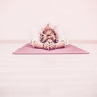 Person in a yoga pose on a pink mat with a pink background