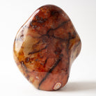A polished, organic-shaped carnelain stone free form with a marbled pattern of brown, amber, and cream, standing upright on a white background.