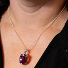 Person wearing a necklace with a purple Amethyst pendant against a black shirt.