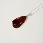 Teardrop-shaped amber pendant on a silver chain against a white background