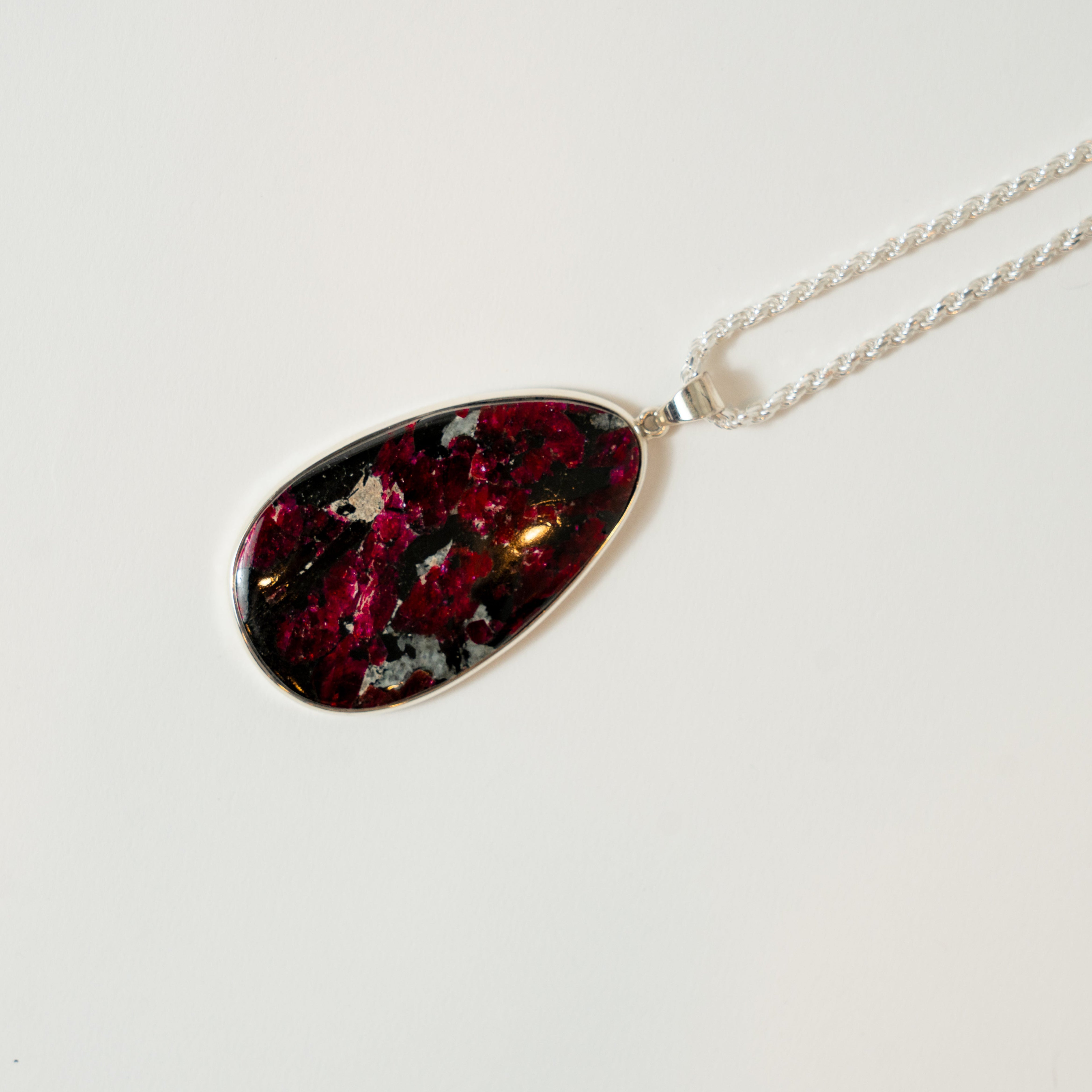 Teardrop-shaped pendant with a red and black pattern on a silver chain against a white background