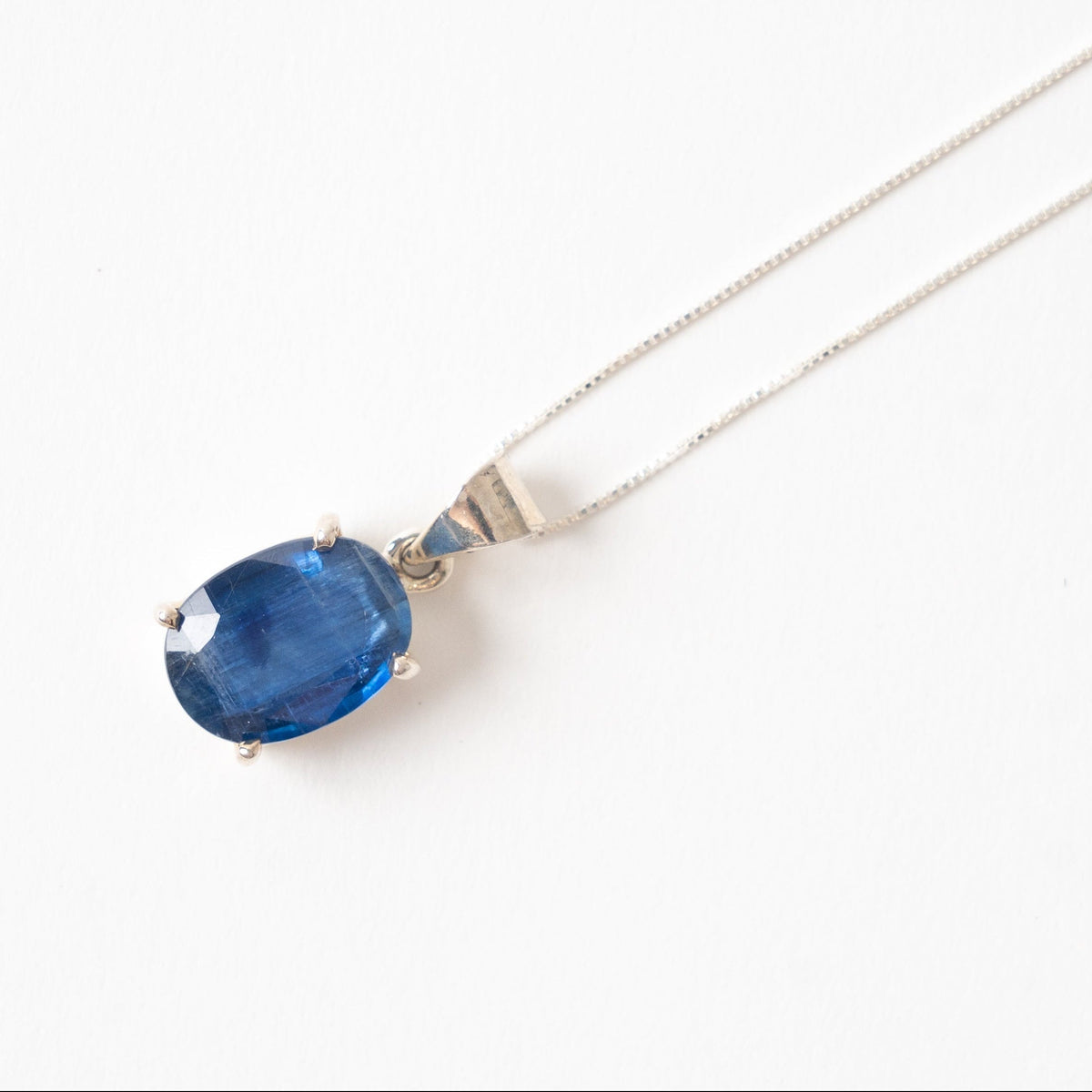 A silver chain necklace with an oval blue kyanite gemstone pendant, photographed on a clean white background.
