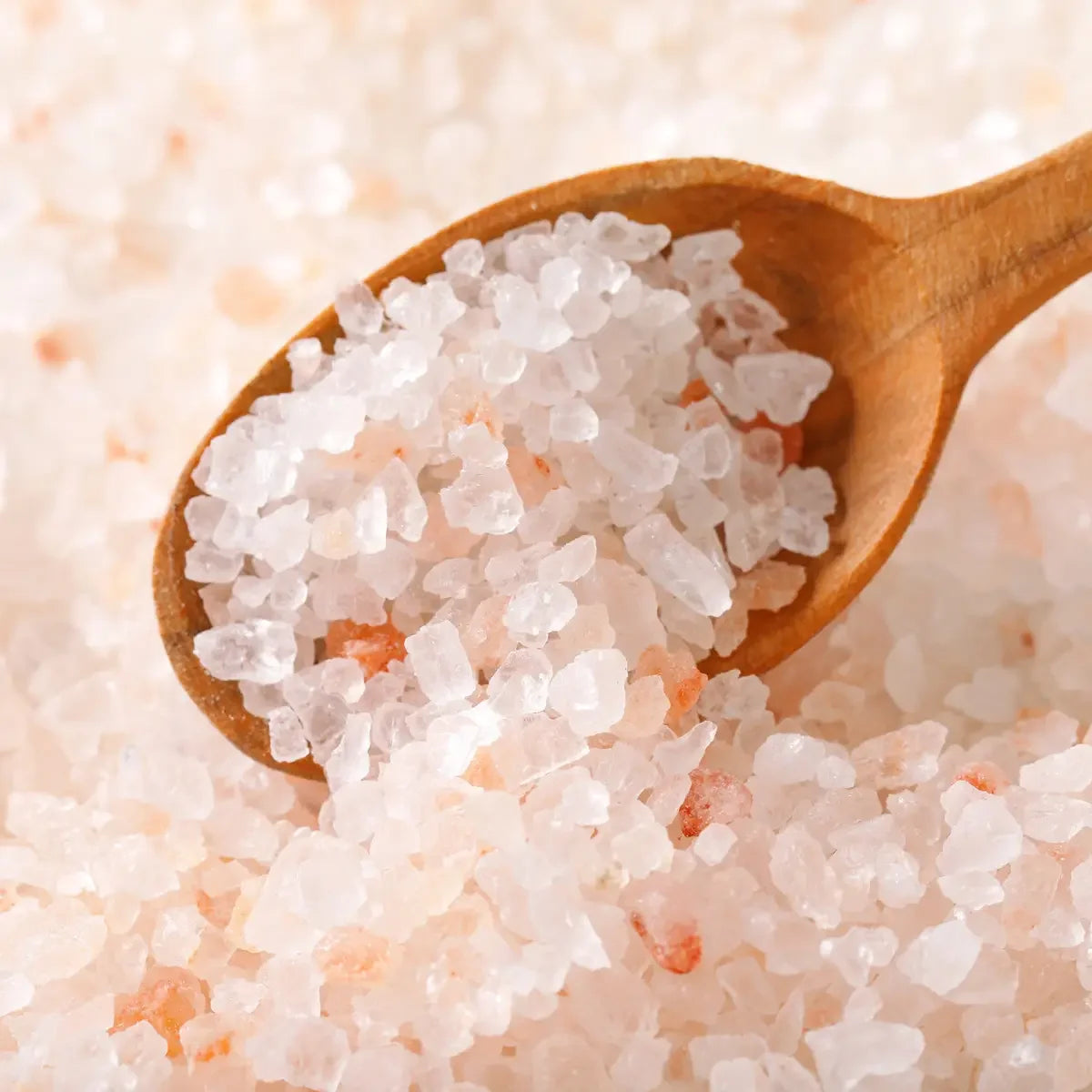 Wooden spoon filled with pink Himalayan salt crystals on a bed of salt.