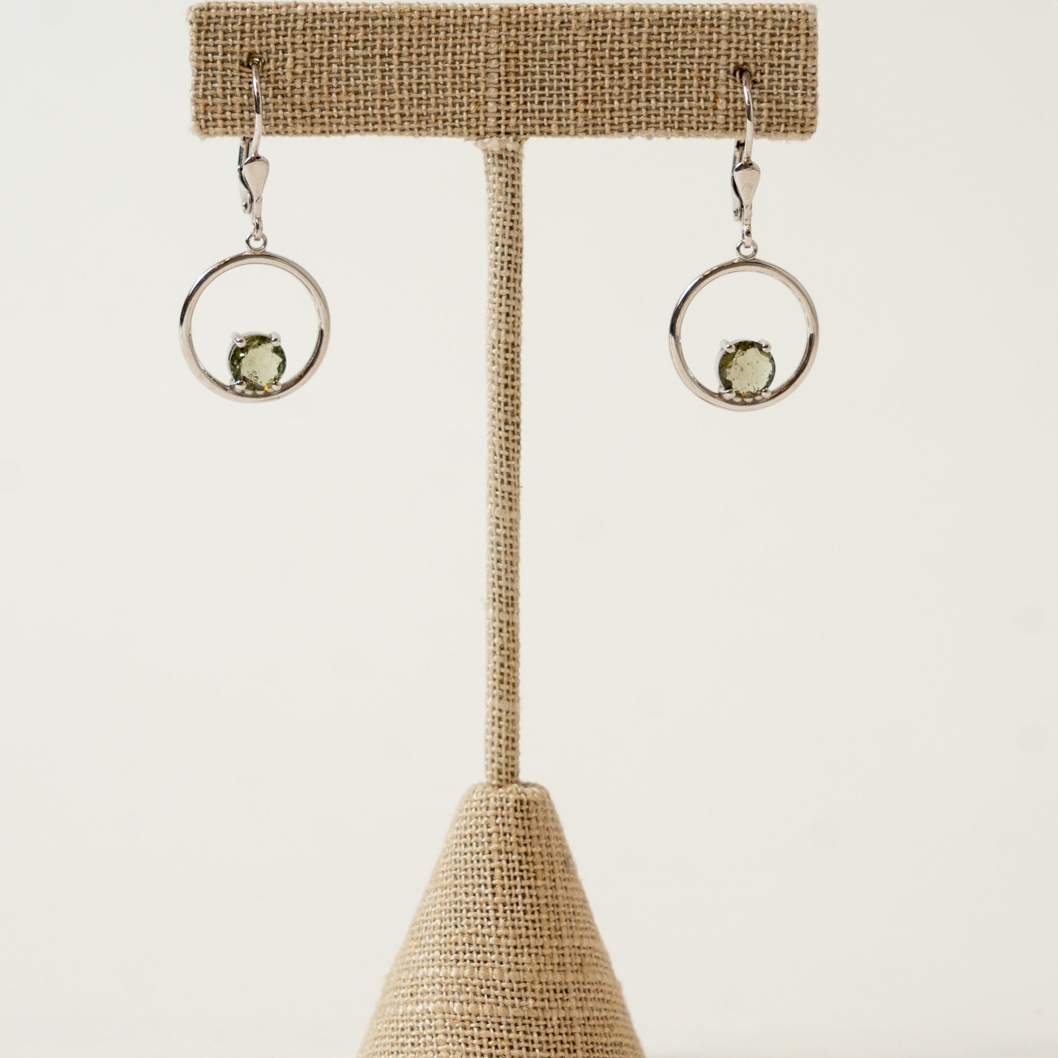 Pair of Moldavite earrings on a decorative stand against a plain background