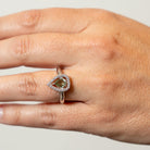 Hand wearing a ring with a green Moldavite gemstone on a neutral background