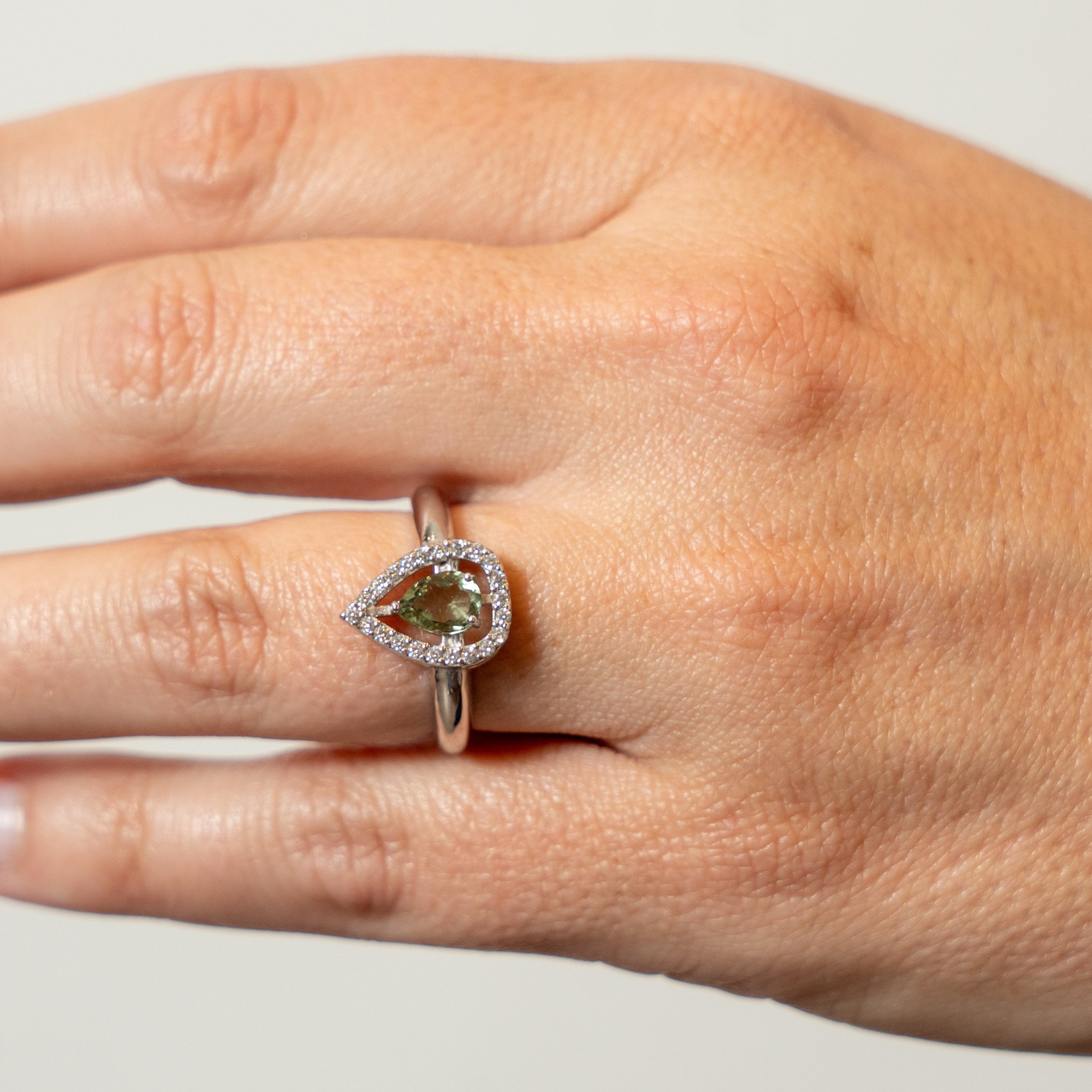 Hand wearing a ring with a green Moldavite gemstone on a neutral background