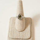 Moldavite and White Topaz Ring on a textured stand with a matching pouch on a light background
