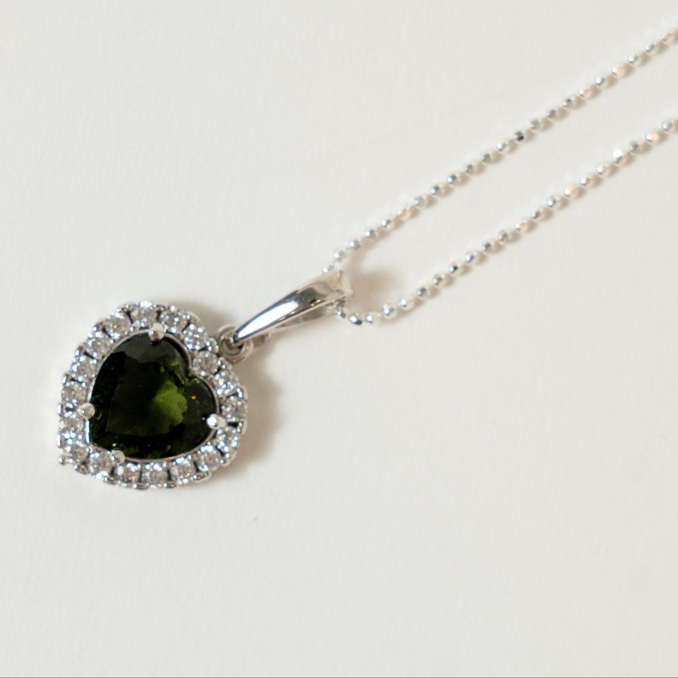 Necklace with a heart-shaped green Moldavite gemstone pendant on a light background