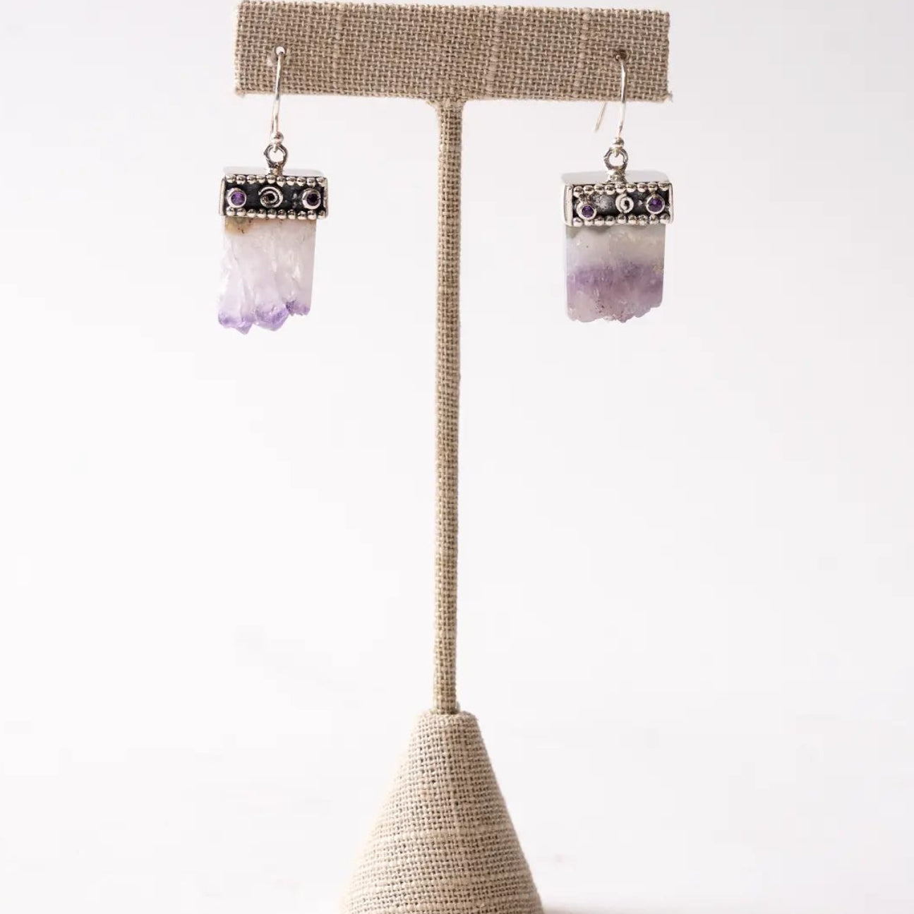 Pair of Amethyst Slice earrings on a beige stand against a white background