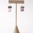 Pair of Amethyst Slice earrings on a beige stand against a white background