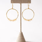 Gold hoop earrings with bead accents on a beige stand against a white background