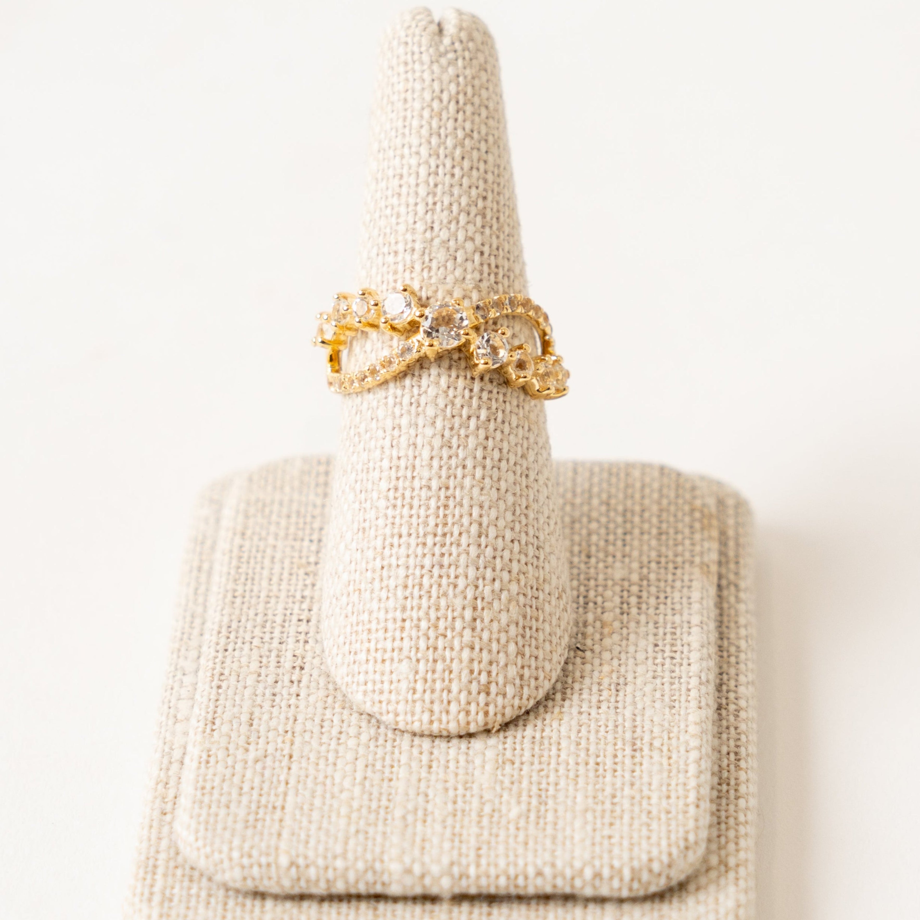 Gold ring with faceted white topaz on a beige ring holder against a white background
