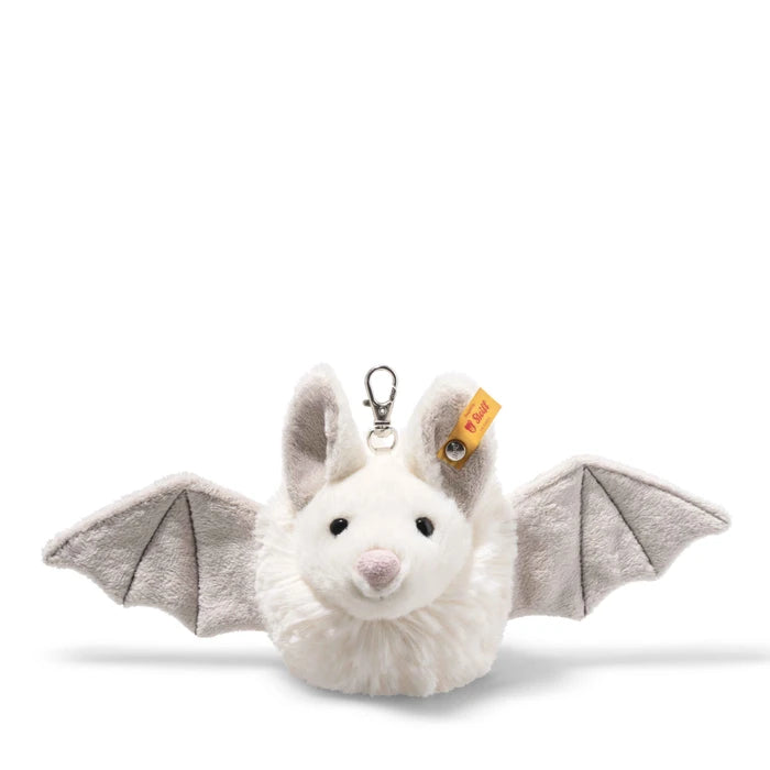 A plush bat keychain or bag charm with outstretched gray wings, a white furry body, black bead eyes, a pink nose, and a silver metal clasp. A small orange tag is attached near the ear.