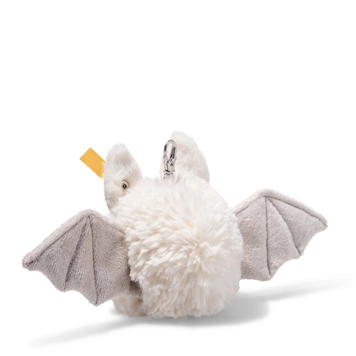 A plush bat keychain or bag charm with fluffy white fur, gray wings, and a small yellow tag, photographed on a clean white background.