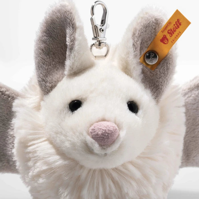 A close-up of a plush bat keychain with a white face, gray wings, and a small orange tag that reads 'Siegfried' and 'Handmade in Germany'.
