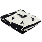 A folded knit blanket featuring a black and off-white pattern of stylized bats and abstract shapes, shown on a plain white background.