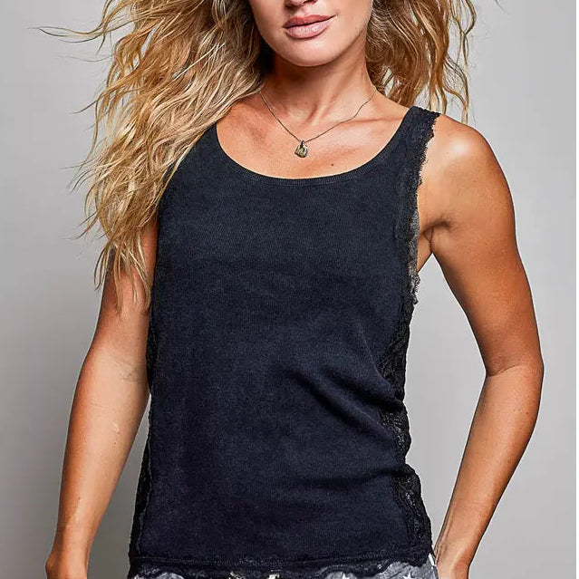 black lace and knit sleeveless tank top with textured, frayed edges and lace trim along the sides, paired with gray patterned pants, against a solid gray studio background.