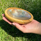 Hand holding a wooden bowl with a shell inside on grass