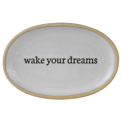 An oval white ceramic tray with a natural beige rim and the phrase 'wake your dreams' printed in black lowercase serif text across the center, shown on a plain white background.