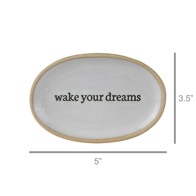 An oval white ceramic tray with a natural beige rim and the phrase 'wake your dreams' printed in black in the center. Dimension lines indicate a width of 5 inches and a height of 3.