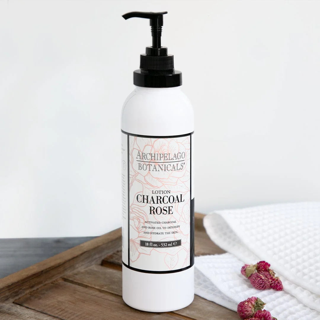 White lotion bottle with pump labeled 'Archipelago Botanicals Charcoal Rose' on a wooden surface.