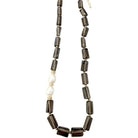 A beaded necklace featuring dark brown translucent rectangular smoky quartz beads, a single white pearl bead, and small gold spacer rings, displayed on a clean white background.