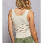 A woman shown from the back wearing a cream-colored ribbed tank top with delicate lace trim along the scoop neckline, paired with green patchwork shorts against a neutral gray studio background.