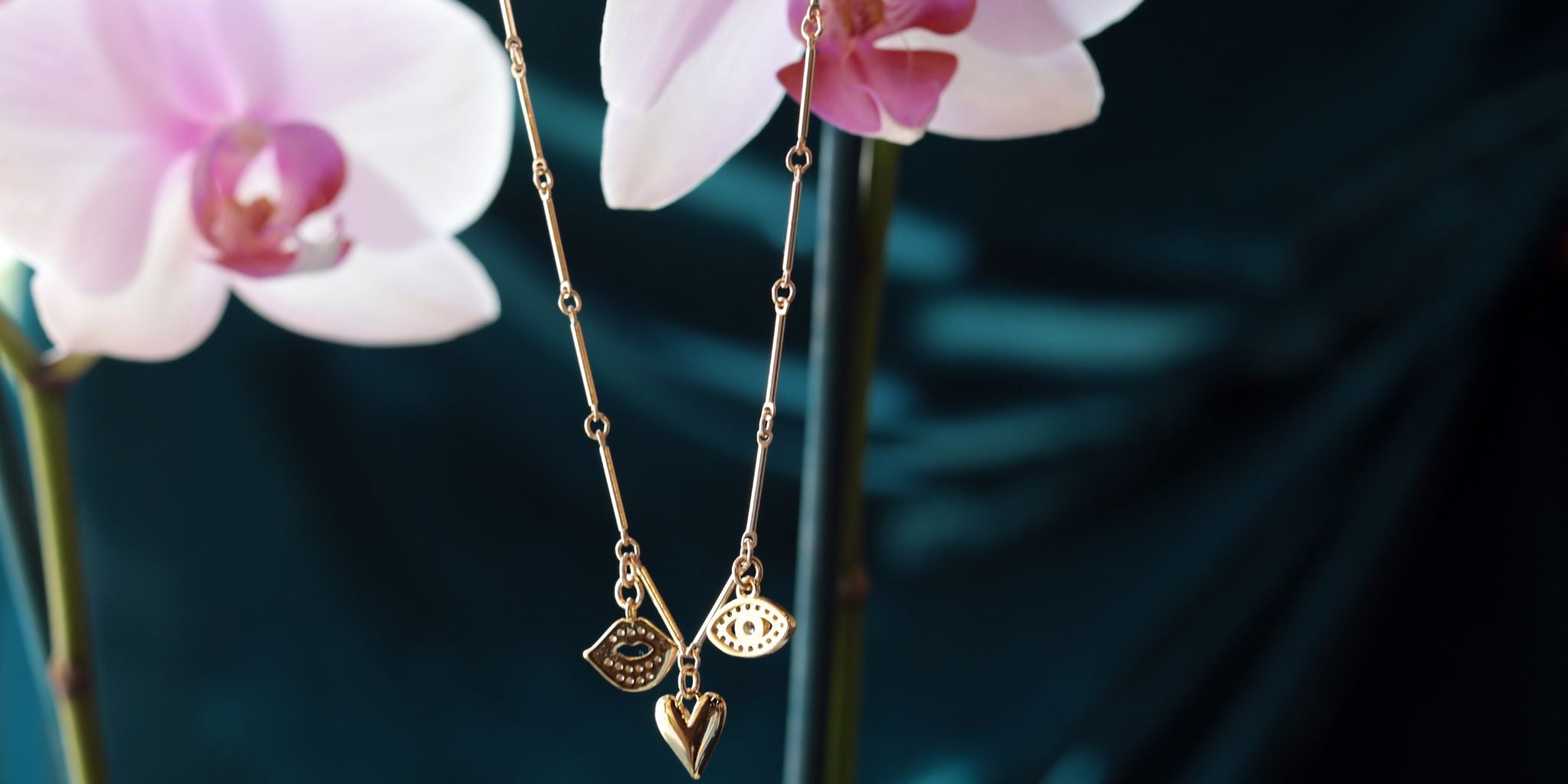 Gold necklace with heart and leaf pendants in front of pink orchids