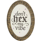 Oval wall art with an ornate antique gold frame and the phrase 'don't hex my vibe' in dark gray script on a white background, accented with small purple sparkles.