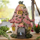 Decorative fairy house with pink roof and yellow windows on a wooden surface.