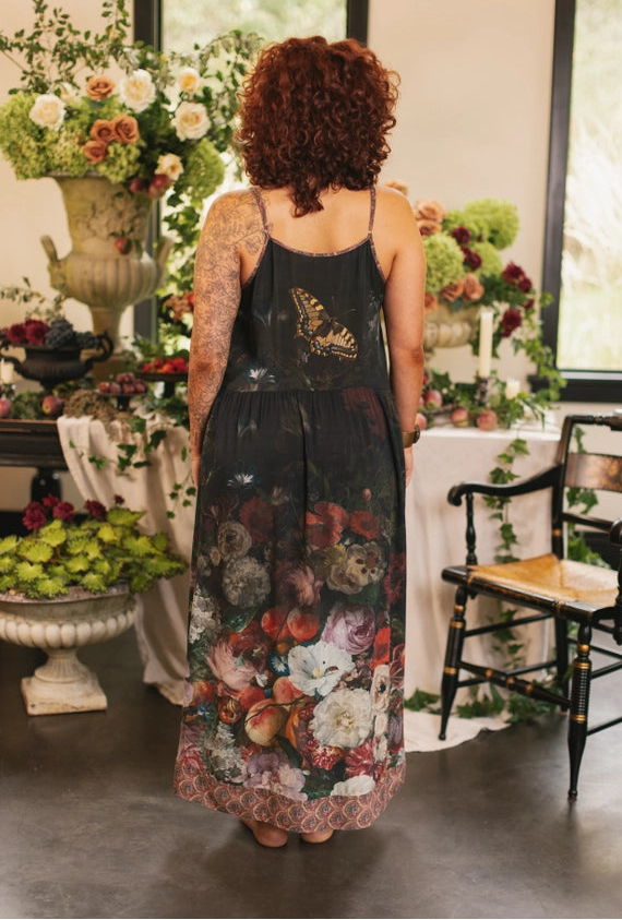 Woman wearing a floral dress standing in a decorated room with flowers and furniture.