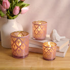 Decorative candle holders with pink and gold patterns on a wooden surface with books and flowers.