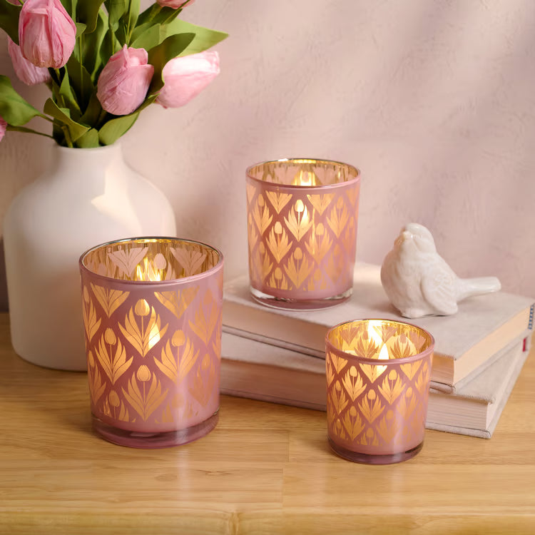 Decorative candle holders with pink and gold patterns on a wooden surface with books and flowers.