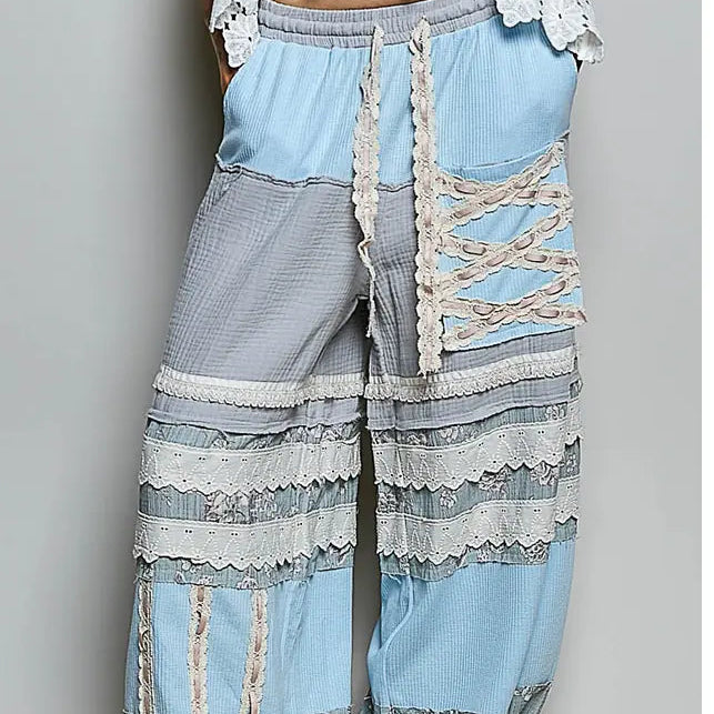 Light blue and gray patchwork wide-leg harem pants with lace trim and side lace-up details, shown on a model wearing gray flip-flops against a neutral gray background.