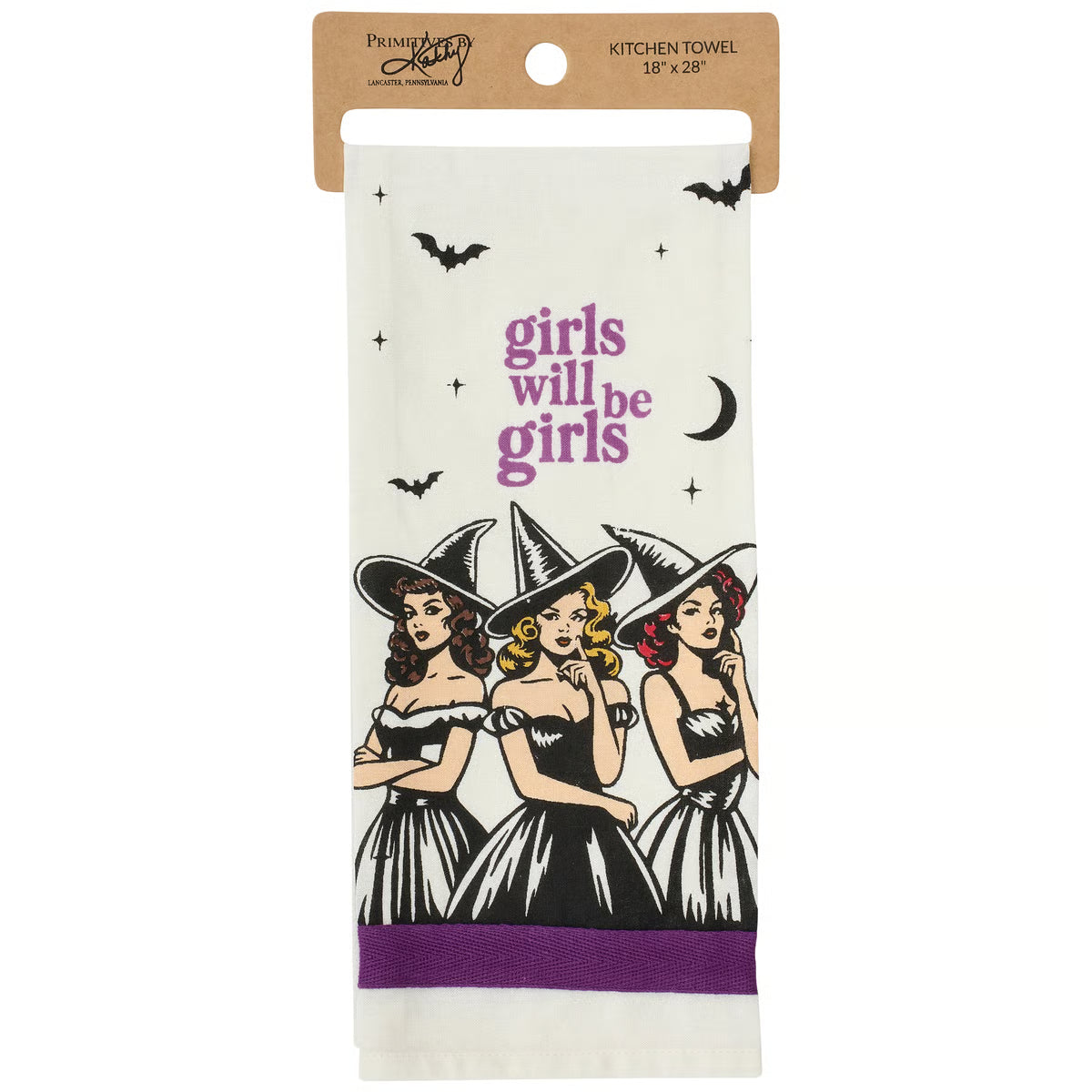 A hanging kitchen towel with a kraft header card. The towel is off-white with a purple and black graphic of three witches and the text 'girls will be girls,' plus small black bat and moon illustrations.