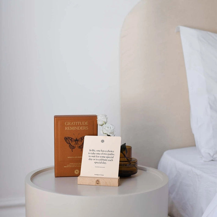 Small round table with books and a card next to a bed with white bedding.
