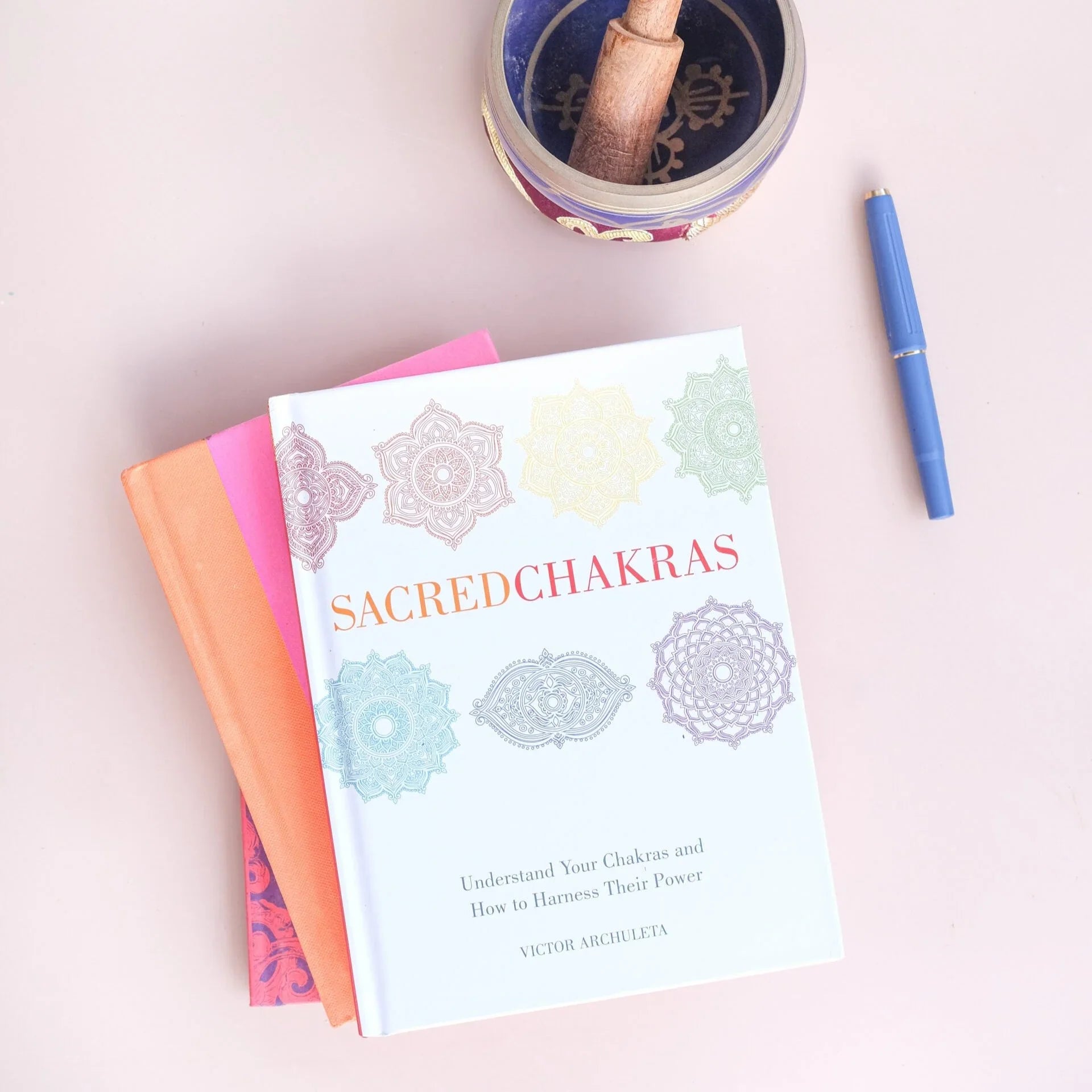 Book titled 'Sacred Chakras' on a light pink background with a pen and container.