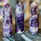 Three amethyst crystal towers on a dark surface with a blurred background