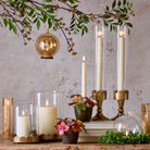 Decorative setup with ivory and gold tea light ornament with flowers, and branches on a textured wall background