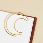 Gold crescent moon-shaped book mark on a white book with a beige background