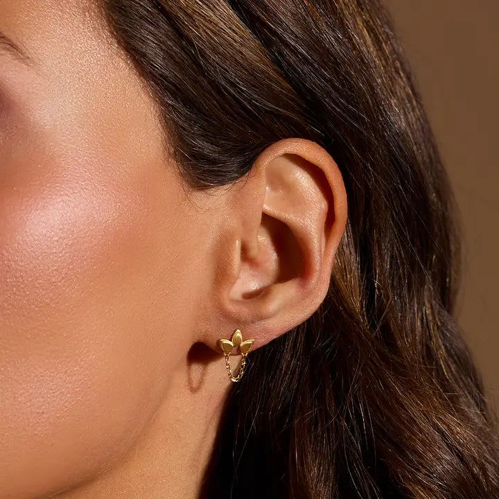 Close-up of a person wearing a gold Lotus Drape Chain Earring with a brown background