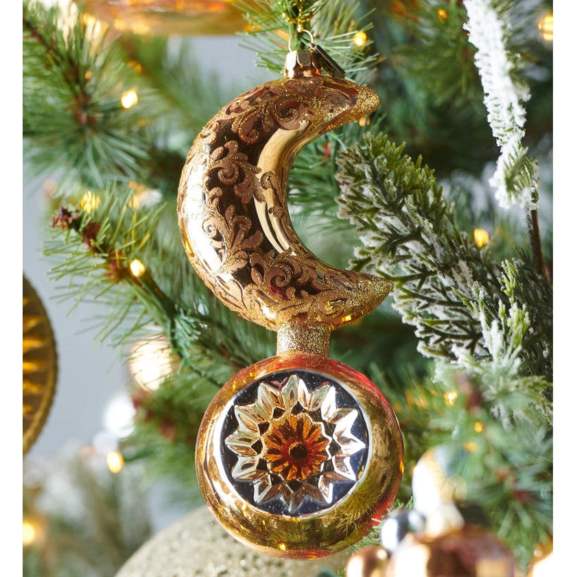 A decorative crescent moon and star Christmas ornament hanging on a decorated Christmas tree. The ornament features an ornate gold crescent moon with carved scrollwork and a matching round star with a floral mandala design in gold, bronze, and silver tones.