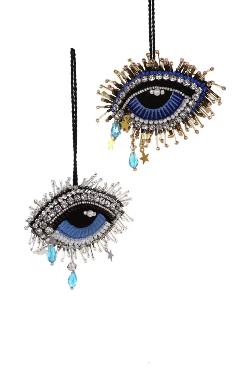 Decorative evil eye with eye lashes charm with blue centers and gold accents on a white background