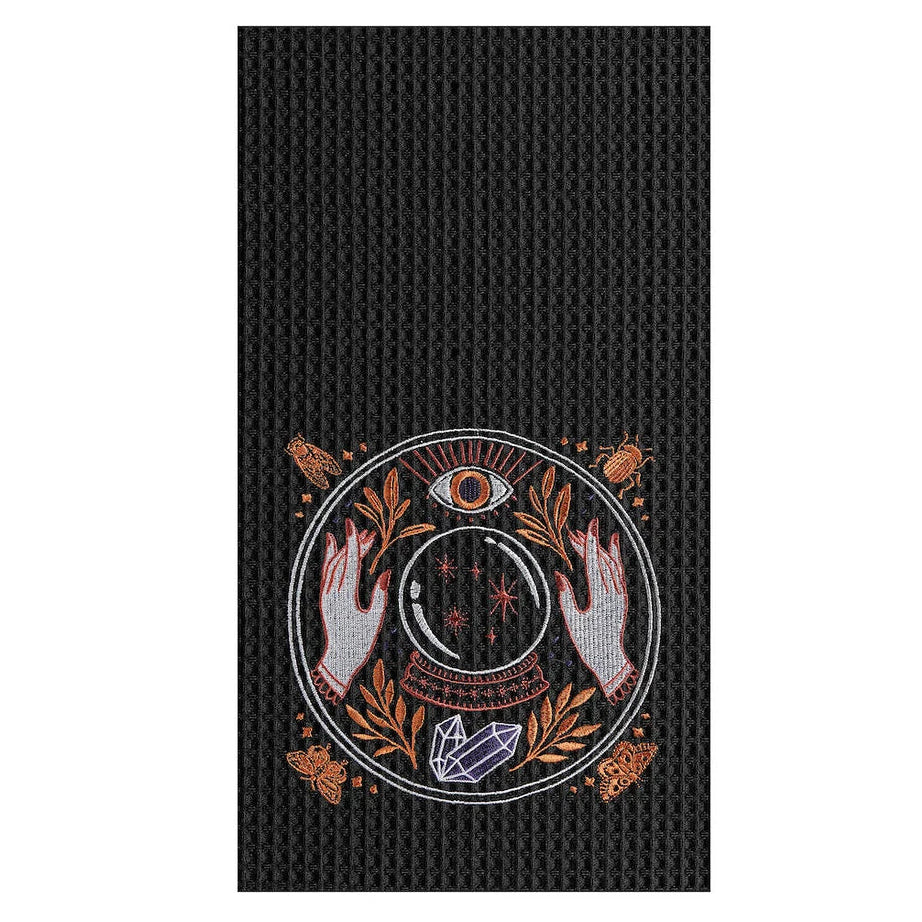 A black textured tea towel featuring a central circular mystical graphic with a triple-eye motif, hands, crystals, and butterflies in muted orange, white, and red tones.