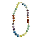A heart-shaped gemstone beaded necklace arranged in an oval shape on a plain white background. The beads transition through multiple colors including green, blue, purple, brown, and yellow, separated by small gold spacer beads and clasp.