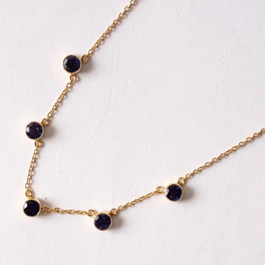 Gold necklace with Iolite gemstones on a white background