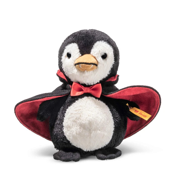 A plush penguin toy dressed as a vampire, featuring black and white fur, a red cape with red lining, a red bow tie, and a yellow beak. A small yellow tag with the Steiff brand logo is visible on the cape.